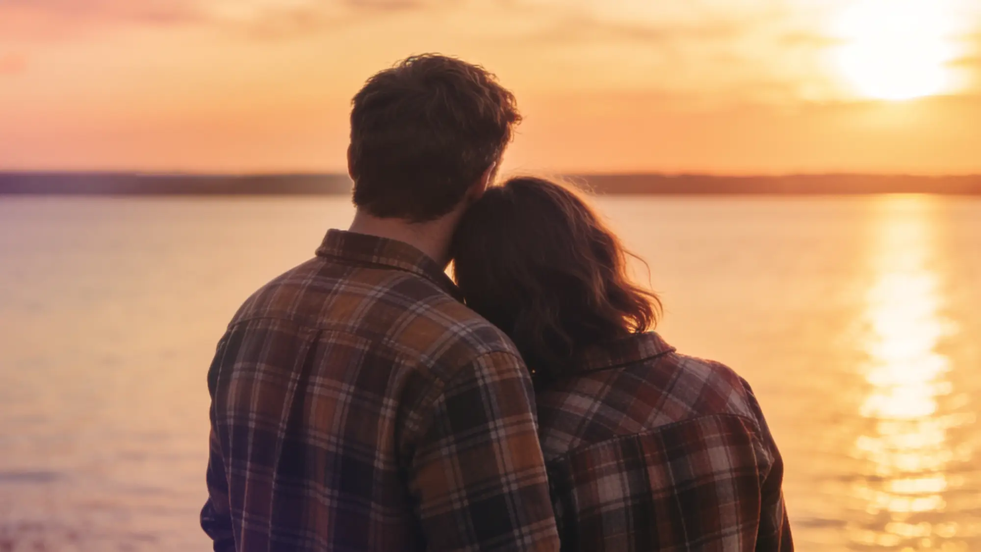 A man and a woman looking out over a lake, towards the sunset